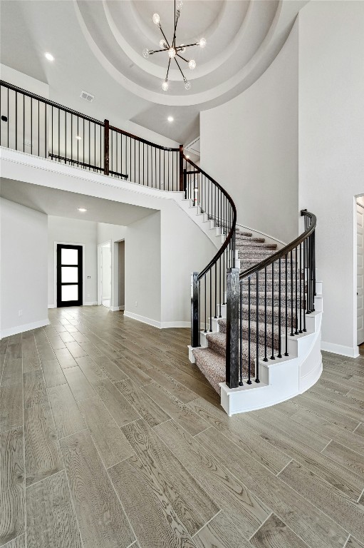 staircase with baseboards, wood finished floors, visible vents, and an inviting chandelier