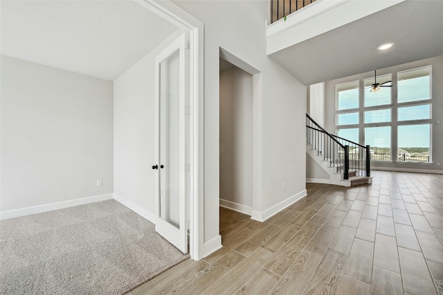 interior space featuring light wood-style flooring, stairway, a towering ceiling, and baseboards