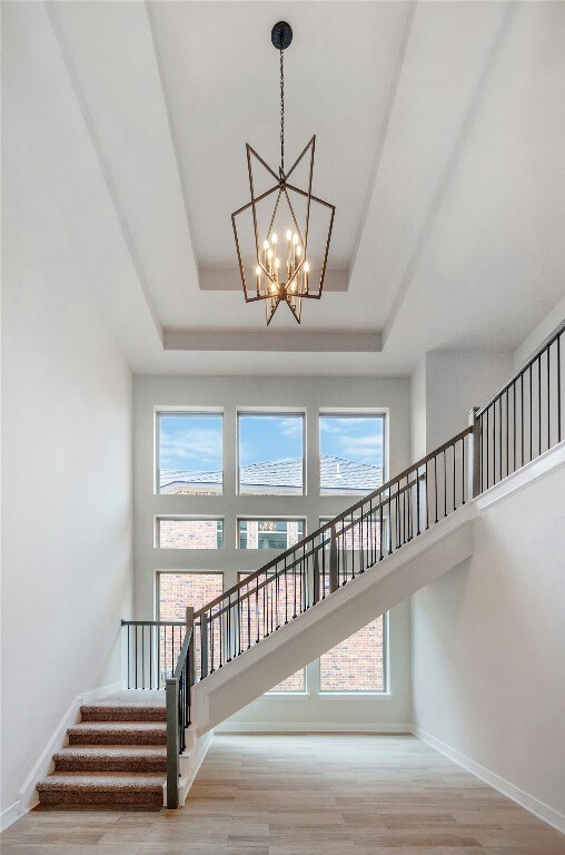 stairs featuring baseboards, wood finished floors, a raised ceiling, a high ceiling, and a notable chandelier