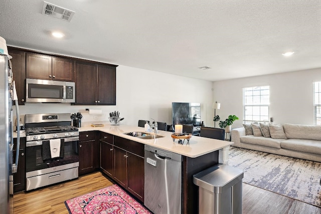 kitchen featuring sink, dark brown cabinets, stainless steel appliances, kitchen peninsula, and light wood-type flooring