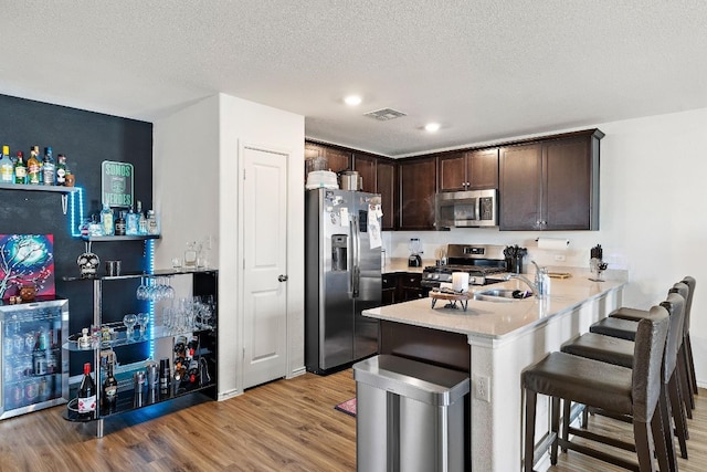 13413 Mussel Run, Elgin, TX 78621 - kitchen featuring stainless steel appliances, dark brown cabinets, a peninsula, light wood-style flooring, and a kitchen bar