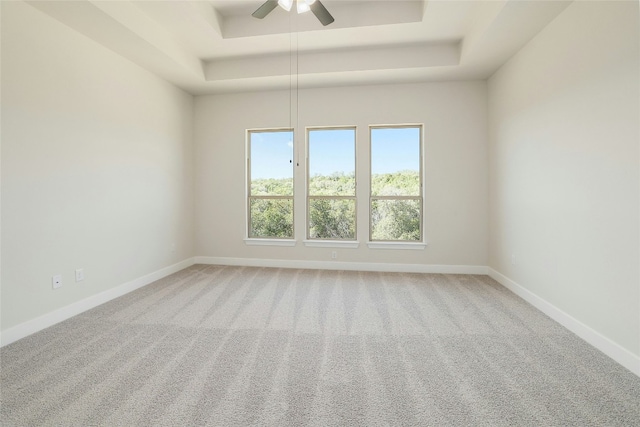 empty room featuring light carpet, baseboards, a tray ceiling, and ceiling fan