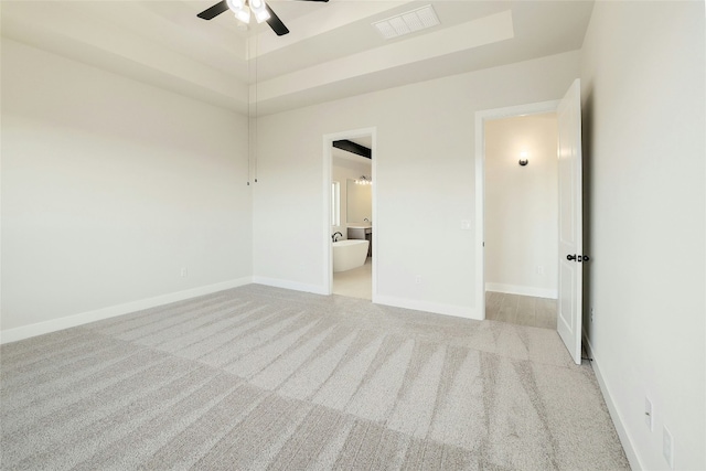 unfurnished bedroom featuring visible vents, baseboards, a raised ceiling, ensuite bathroom, and carpet