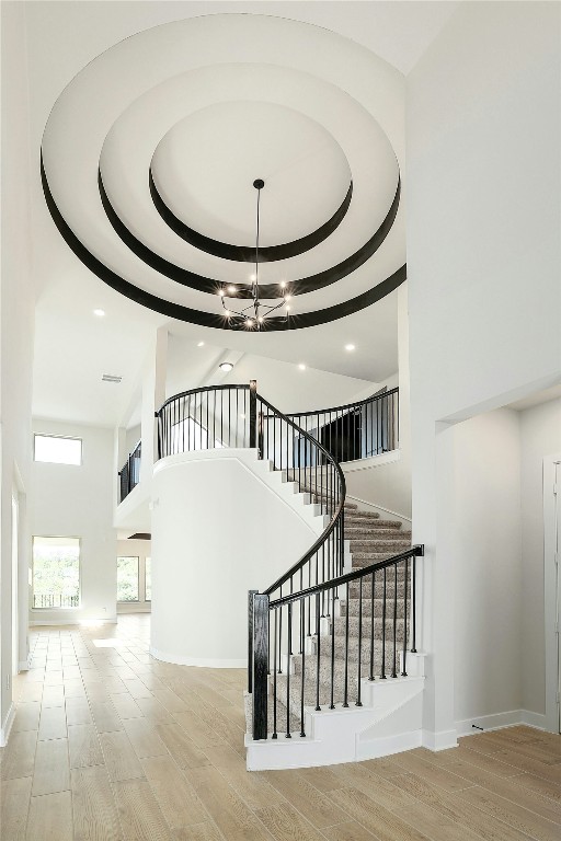 staircase featuring baseboards, a raised ceiling, a towering ceiling, wood finished floors, and an inviting chandelier