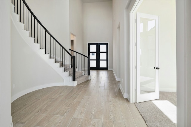 entrance foyer with baseboards, wood finished floors, stairs, a high ceiling, and french doors