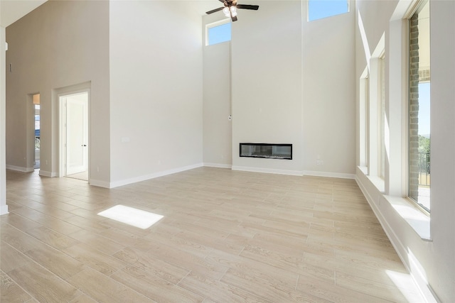 unfurnished living room with light wood-style flooring, baseboards, a ceiling fan, and a glass covered fireplace