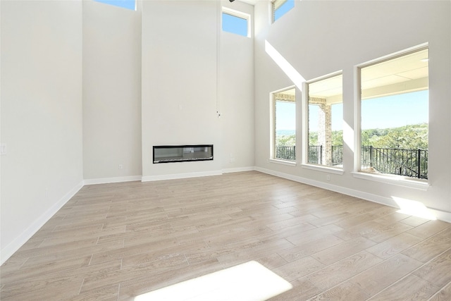 unfurnished living room with light wood finished floors, a glass covered fireplace, and baseboards