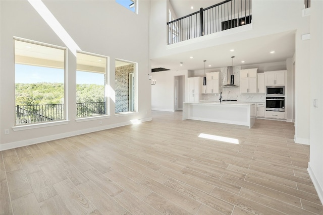 unfurnished living room featuring baseboards, recessed lighting, a sink, and light wood-style floors