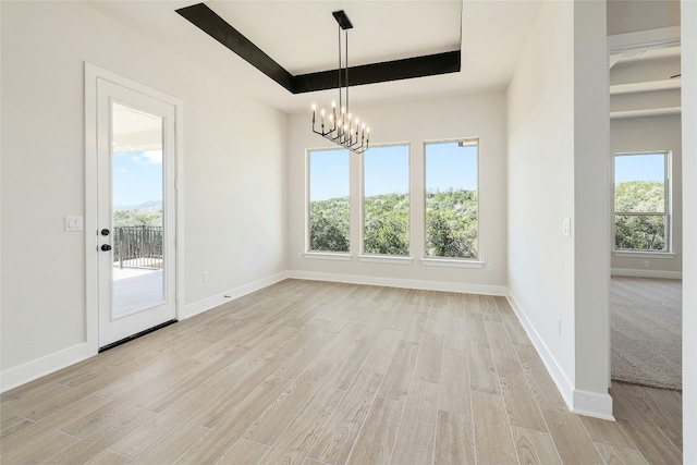 unfurnished dining area with a raised ceiling, baseboards, and light wood finished floors