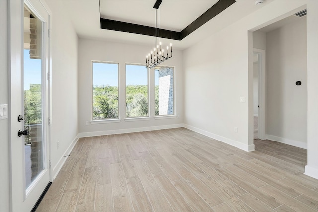 empty room with light wood-type flooring, visible vents, and a raised ceiling