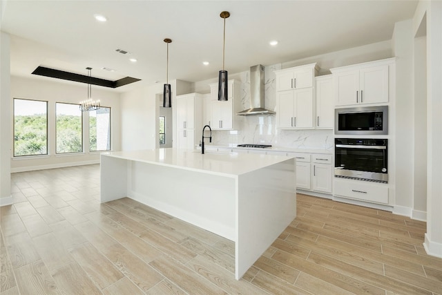 kitchen featuring wood finish floors, tasteful backsplash, a raised ceiling, appliances with stainless steel finishes, and wall chimney exhaust hood