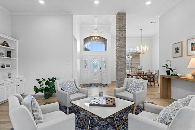 living room featuring an inviting chandelier, ornamental molding, light hardwood / wood-style floors, and decorative columns