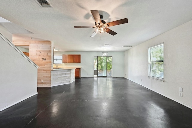 unfurnished living room featuring ceiling fan, a textured ceiling, a healthy amount of sunlight, and wood walls