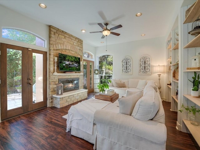 living room with french doors, ceiling fan, dark hardwood / wood-style flooring, and a stone fireplace