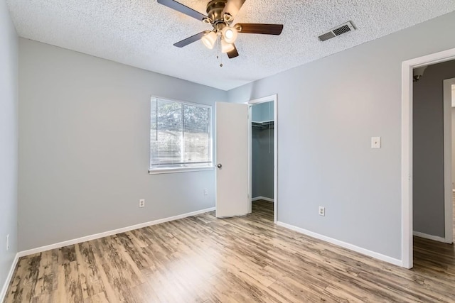 unfurnished bedroom featuring light hardwood / wood-style flooring, ceiling fan, a textured ceiling, a spacious closet, and a closet