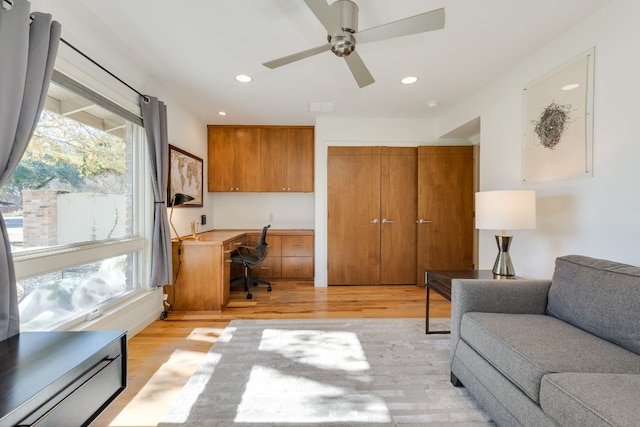 living room with ceiling fan, built in desk, light hardwood / wood-style flooring, and a wealth of natural light