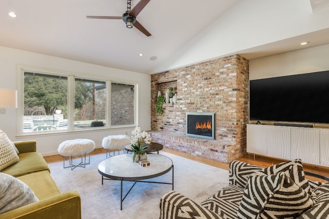 living room with a brick fireplace, high vaulted ceiling, ceiling fan, and light wood-type flooring