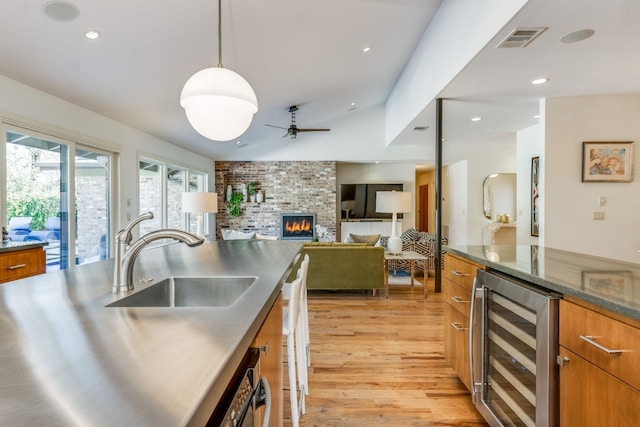 kitchen featuring sink, a brick fireplace, hanging light fixtures, light wood-type flooring, and beverage cooler