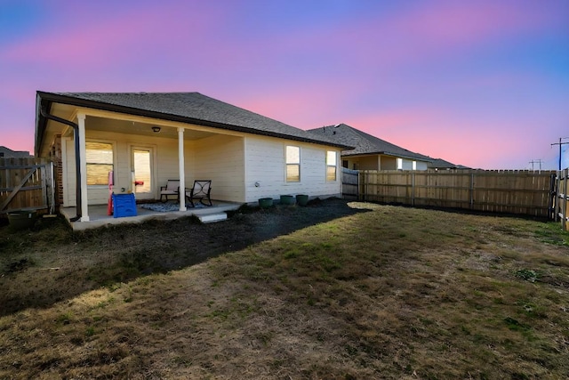 back house at dusk featuring a patio and a yard