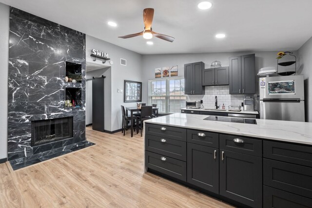 kitchen featuring light stone countertops, stainless steel fridge, light wood-type flooring, and decorative backsplash