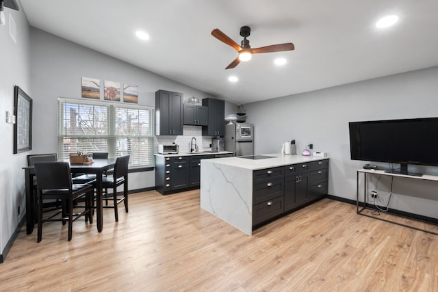 kitchen featuring vaulted ceiling, sink, backsplash, and light wood-type flooring