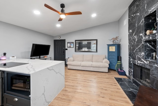 living room with ceiling fan, lofted ceiling, a fireplace, and light hardwood / wood-style floors