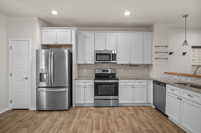 kitchen featuring light stone countertops, appliances with stainless steel finishes, white cabinets, and decorative light fixtures