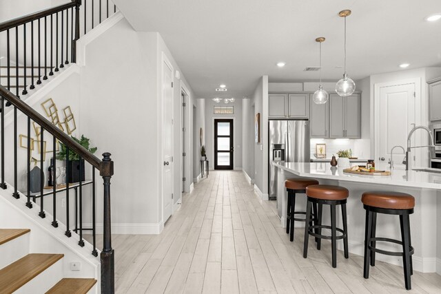 kitchen with a breakfast bar, decorative light fixtures, gray cabinets, stainless steel appliances, and backsplash