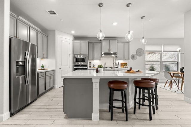 kitchen with a breakfast bar, pendant lighting, gray cabinetry, stainless steel appliances, and a center island with sink