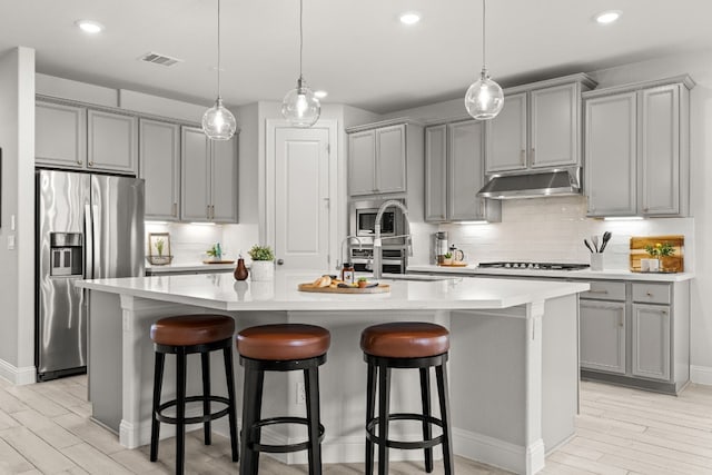 kitchen featuring a kitchen island with sink, a kitchen bar, gray cabinetry, and appliances with stainless steel finishes