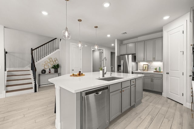 kitchen with sink, hanging light fixtures, a center island with sink, gray cabinets, and stainless steel appliances