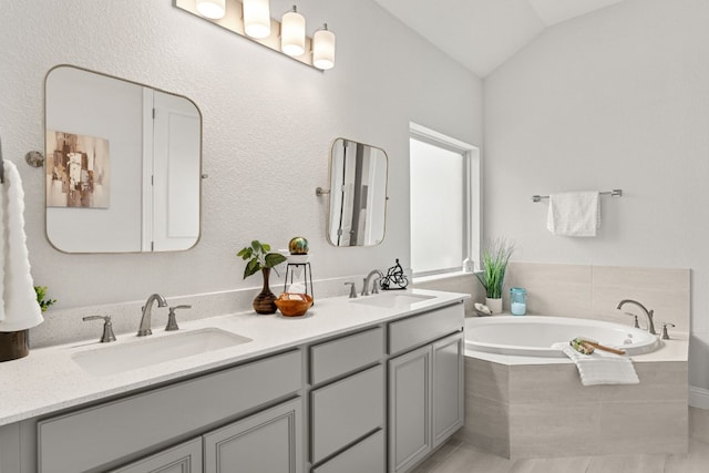 bathroom featuring vanity, lofted ceiling, and tiled bath