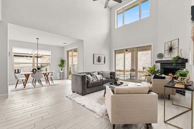 living room featuring a towering ceiling, a tiled fireplace, and ceiling fan with notable chandelier