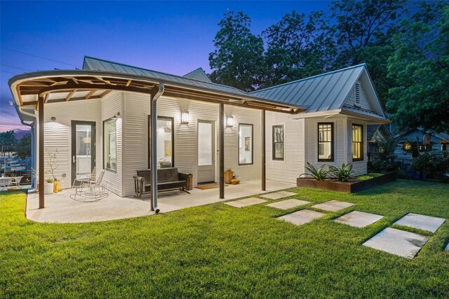 back house at dusk featuring a patio and a lawn