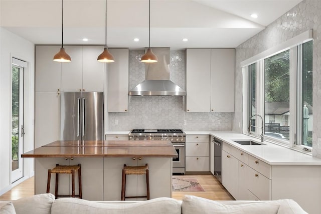 kitchen featuring decorative light fixtures, sink, premium appliances, light hardwood / wood-style floors, and wall chimney range hood