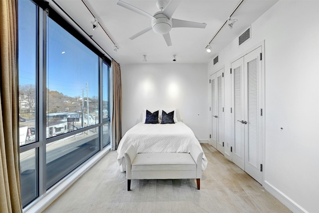 bedroom with ceiling fan, rail lighting, a wall of windows, and two closets