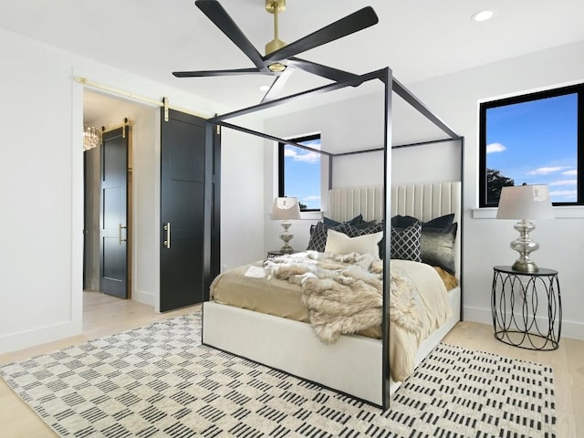 bedroom with ceiling fan, a barn door, a closet, and light wood-type flooring