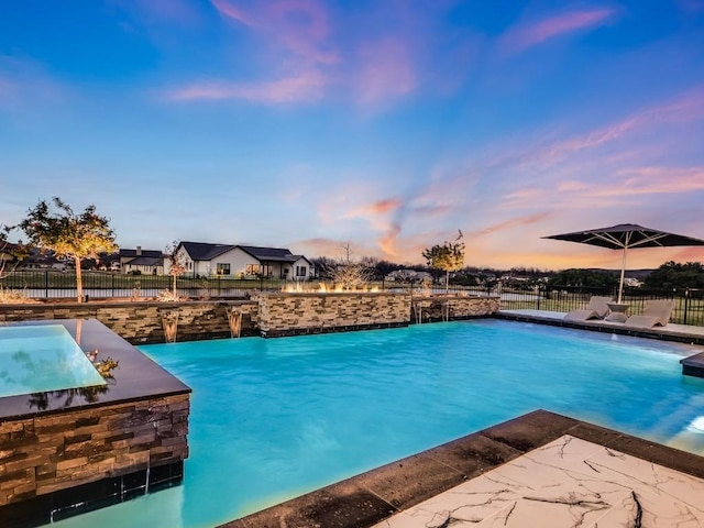 pool at dusk with pool water feature and a patio area