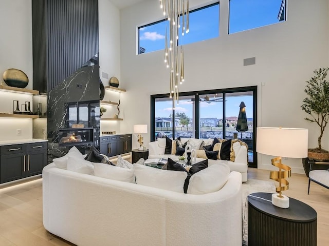 living room with a high ceiling, a wealth of natural light, a high end fireplace, and light hardwood / wood-style flooring