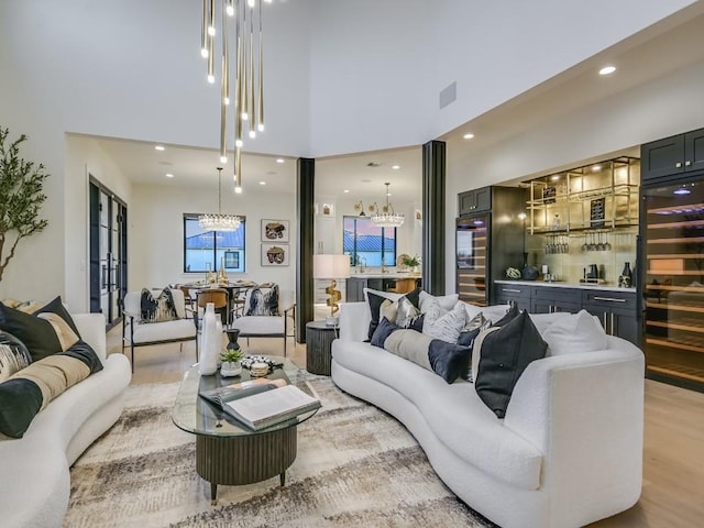 living room featuring a towering ceiling, beverage cooler, a chandelier, and light wood-type flooring