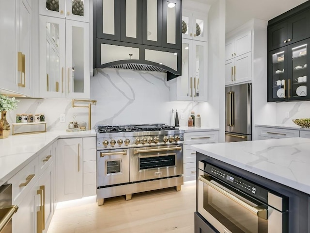 kitchen with high end appliances, light stone countertops, white cabinets, and light wood-type flooring