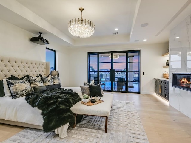 bedroom featuring access to exterior, a tray ceiling, light hardwood / wood-style floors, and a chandelier