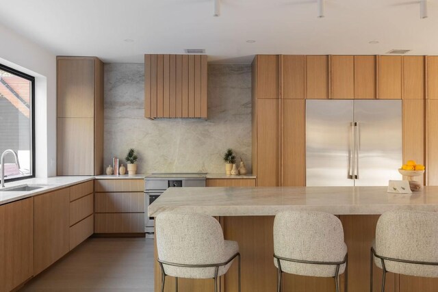 kitchen with built in fridge, a breakfast bar, light brown cabinetry, sink, and range