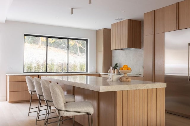 kitchen with light wood finished floors, a center island, stainless steel built in refrigerator, and a breakfast bar