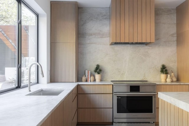 kitchen with a sink, modern cabinets, light brown cabinetry, and stove