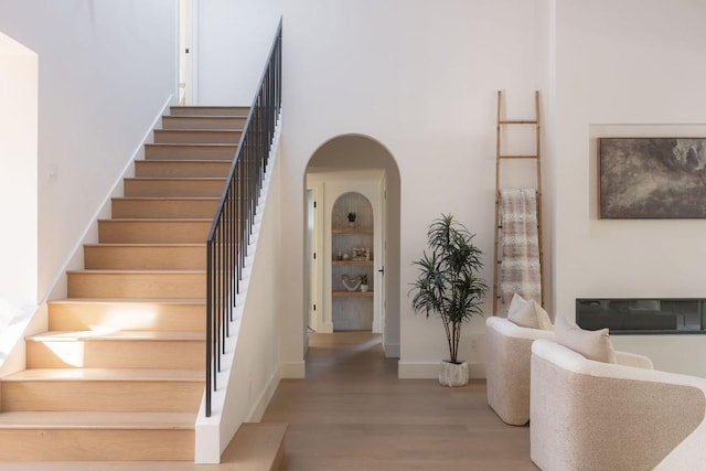 stairs featuring arched walkways, a high ceiling, baseboards, and wood finished floors