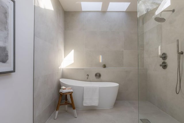 full bath with a skylight, a walk in shower, a soaking tub, and tile walls