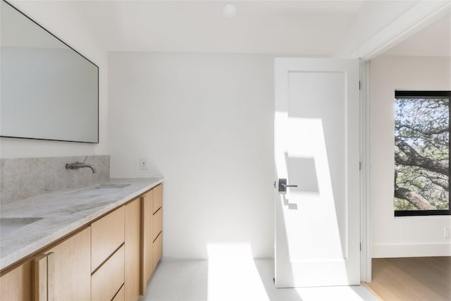 bathroom with double vanity, baseboards, a sink, and wood finished floors