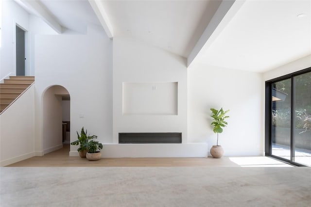 unfurnished living room with arched walkways, lofted ceiling with beams, and stairway