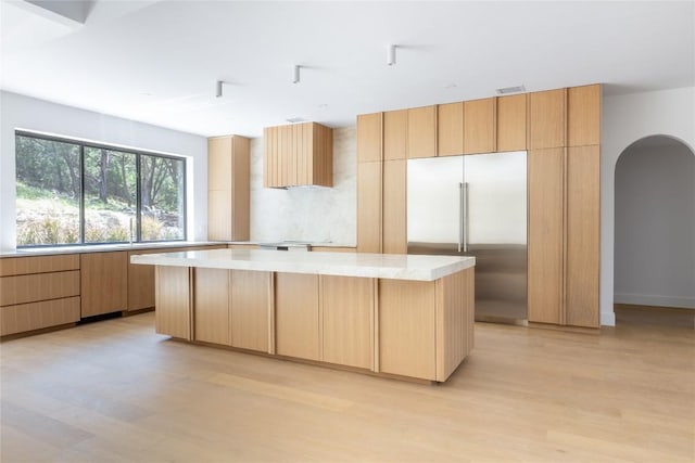 kitchen with light wood-type flooring, arched walkways, a kitchen island, and built in refrigerator